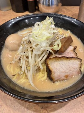 A bowl of Japanese ramen topped with sliced pork, bean sprouts, green onions, a boiled egg, and nori in a creamy broth.