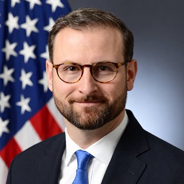 A professional headshot shows a bearded man wearing glasses, a dark suit, white shirt, and blue tie, posing in front of an American flag. The image accompanies a quote attributed to Patrick Witt, identified in the post as White House Digital Assets Adviser, criticizing the Clarity Act vote as a disappointment and failure of American leadership.