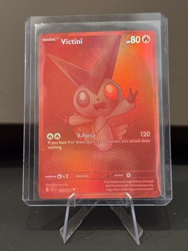A holographic/rainbow foil Pokémon card featuring Victini (#25) with 80 HP, displaying the 'V-Force' attack that does 120 damage if heads. The card is encased in a protective sleeve and displayed on a small stand.