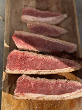 Slices of rare, pink-centered steak lined up on a wooden cutting board.