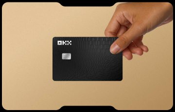 A promotional image showing a hand holding a black OKX-branded credit/debit card against a tan background.