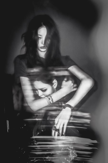 A black and white artistic photo features a woman with long dark hair embracing a reflected or doubled image of herself, creating a dreamlike, distorted double-exposure effect that embodies the piece's title "The Embracing Woman," an NFT artwork shared on objkt.com.