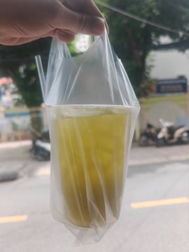 A hand holding up a clear plastic bag filled with a yellow liquid, with a street scene and motorcycles visible in the blurred background.