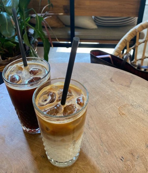 The image features two glasses filled with coffee sitting on a wooden table. The glasses have straws sticking out of them, suggesting they are ready for someone to enjoy their refreshing beverages. In the background, there's a bench where one could sit down and relax while sipping their drink. A potted plant is also visible in the scene, adding some greenery to the space. The image seems to be related to a post on social media, as it includes text that reads "Good Morning Legens while most of the timeline is chasing the next meme, some teams are busy solving problems that haven'nt fully arrived yet that's what keeps me watching @quipnetwork".