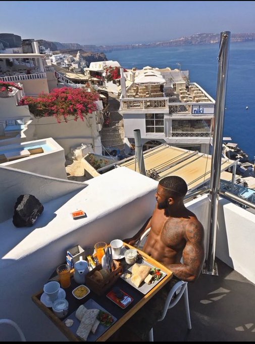 The image shows a man sitting at an outdoor table, which has food and drinks laid out for him. The man appears to be enjoying his meal while overlooking a beautiful view of the ocean from the balcony. The scene also includes several cups, bowls, and other items on the dining table. The post about Dropee app seems to be related to this image as it highlights how the app has gained significant attention due to its ranking high in search results for the #1 hyped pre-TGE launch.