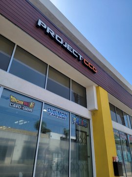 The exterior of a storefront called "Project CC" is shown, featuring Mellow Out (Café/Bar), Chimoy Cake Café, and other tenants visible in the windows. The post humorously references hanging out at a nearby izakaya, with the café/spot serving as a potential meetup location for the group.
