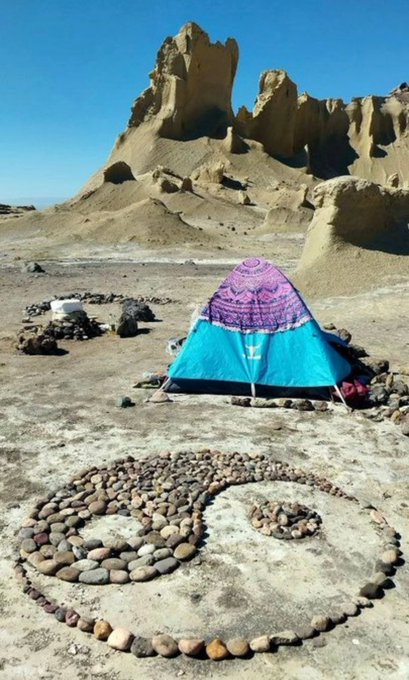 A teal and pink mandala-patterned tent sits in a barren desert landscape, with a spiral of arranged stones forming a yin-yang symbol in the foreground and dramatic eroded rock formations rising in the background. The serene, grounded camping scene complements the post's reflective "good morning" greeting and contemplative tone about keeping watch on sleep rewards and privacy-focused crypto projects.