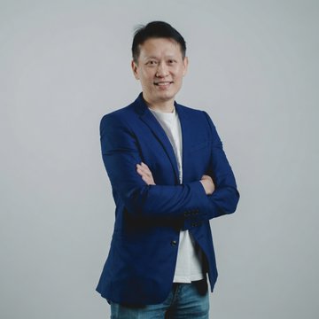 The image shows a man, likely Binance co-CEO Richard Teng, posing confidently with his arms crossed in a blue blazer against a light gray background. This professional portrait accompanies news about his statements at Reuters NEXT Asia regarding Binance EU users shifting to self-custodied wallets following the exchange's failure to secure MiCA authorization.