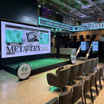 A Bitkub venue features a stage with "METAPLEX" branding displayed on a large screen and overhead signs, surrounded by rows of empty chairs, highlighting the MetaPlex event's recent presence in Thailand.