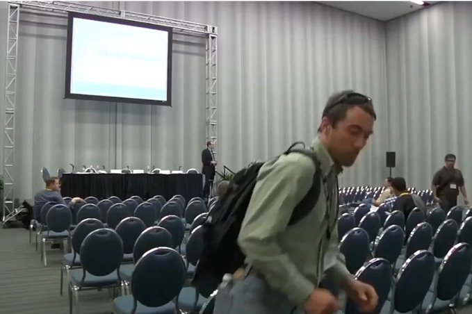 A man wearing a backpack walks through a conference room with rows of empty chairs and a projector screen displaying a presentation, suggesting a quiet moment before an event begins. The image metaphorically represents the calm "before the storm"—much like Ethereum's (ETH) subdued state before its anticipated massive rally, paralleling Bitcoin's (BTC) early days when it was valued at just a few dollars.