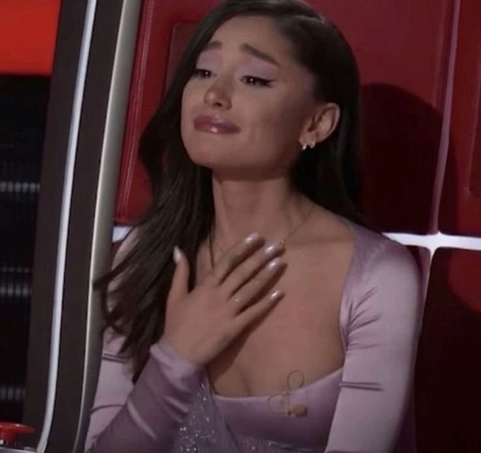 A woman with long dark hair wearing a lavender outfit, appearing emotional with tears, seated in a red chair (likely from a TV show like The Voice).