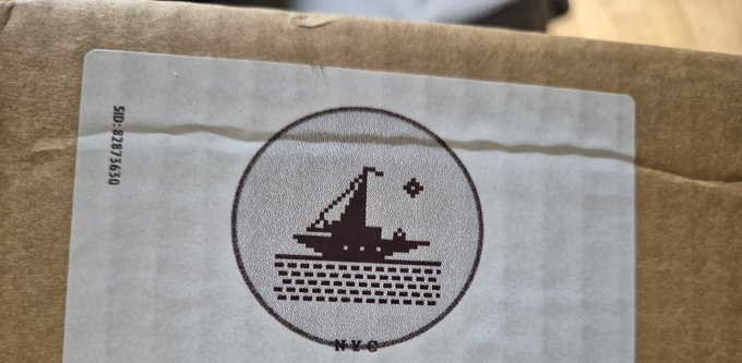 A close-up of a cardboard package shows a circular black stamp featuring a sailboat illustration with 'N.Y.C' beneath it and the code 'SD#28373530' printed vertically on the left.