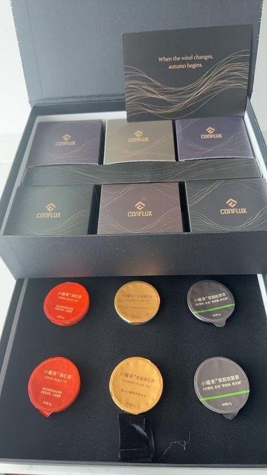 A presentation box from Conflux containing six individually sealed tea pods (red, yellow, and grey) and small packets, with an insert card reading 'When the wind changes, autumn begins.'