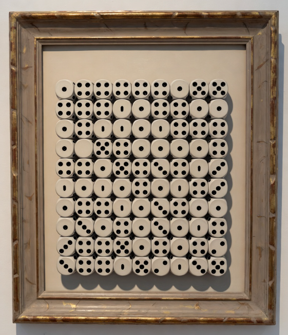 A framed art piece displaying a grid arrangement of white, round, button-like objects with varying numbers of holes in each, mounted on a beige background within a distressed gold frame.