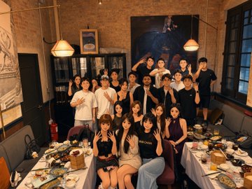 A large group of people posing together at what appears to be a dinner gathering in a restaurant with brick walls and hanging lamps.