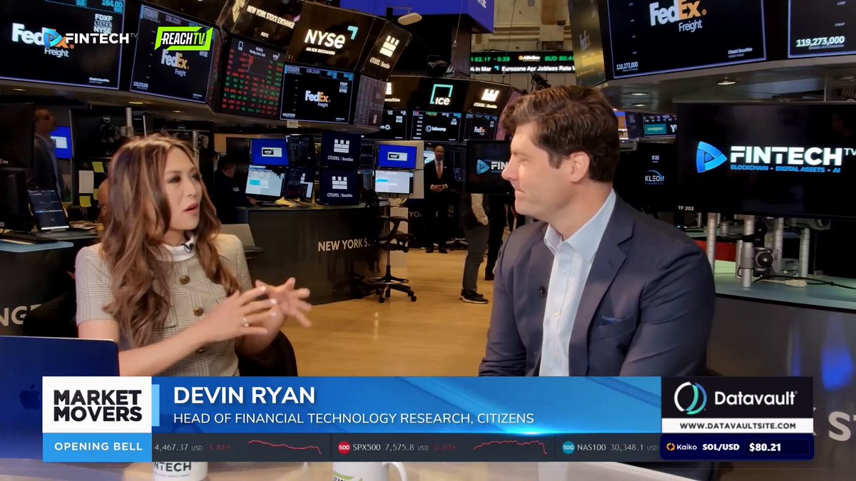 The image shows a man and woman sitting at a desk, talking about financial markets. The woman appears to be an expert or a financial analyst, while the man seems to be interested in learning more about the subject. They are surrounded by multiple screens displaying stock market data, indicating that they might be discussing recent developments in the financial world. The image also includes text elements such as "market moves" and "focus on what is in the image", which could be related to the content of their conversation or the context surrounding it.
