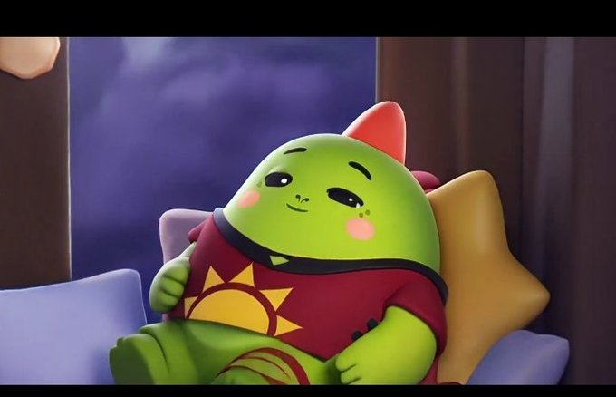 A 3D-rendered cute green cartoon character with pink cheeks wearing a red shirt with a sun design reclines against a pillow.