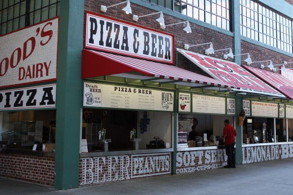 An exterior view of food stands with signs reading 'FOOD'S DAIRY PIZZA' and 'PIZZA & BEER', featuring red and white striped awnings and brick detailing.