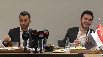 Two men sit at a press conference table with multiple microphones, with a Turkish flag visible on the right.