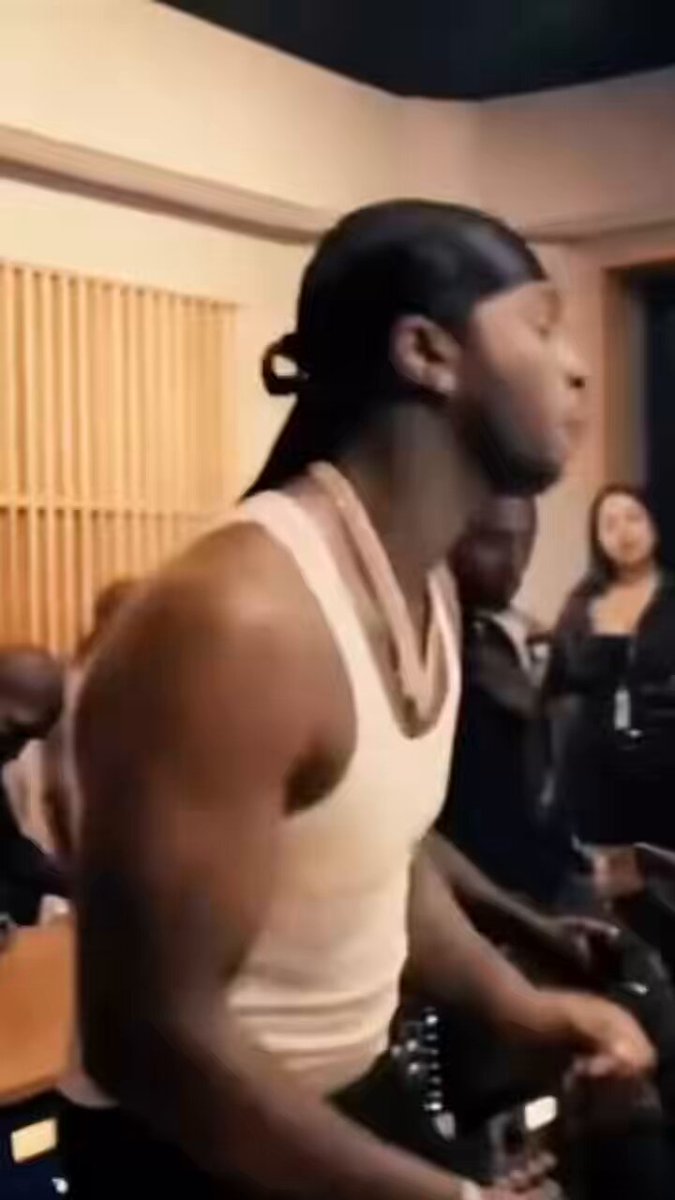 The image features a man with long hair wearing a white tank top, standing in front of a group of people who are watching him intently. He has his arms crossed over his chest as he looks off into the distance. The caption for this image reads "$WOJAK ATH".