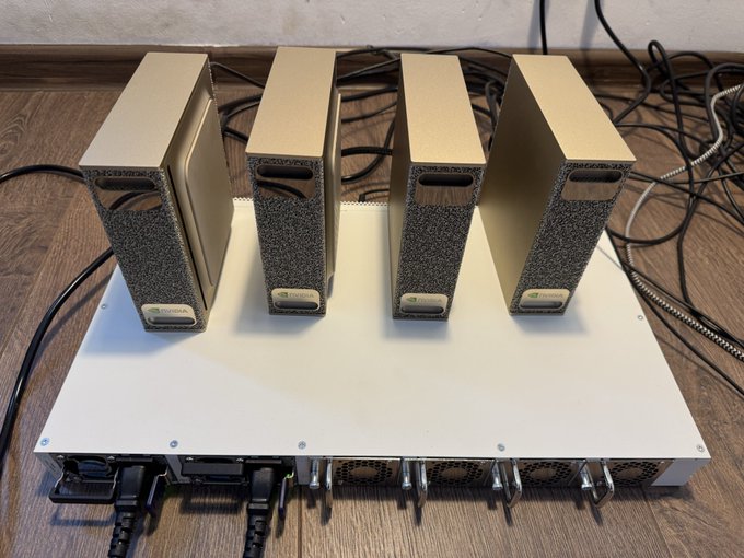A photograph of a white server rack or NAS enclosure sitting on a wooden floor, populated with four vertical hard drive bays with textured gray and gold casings, connected by various cables.