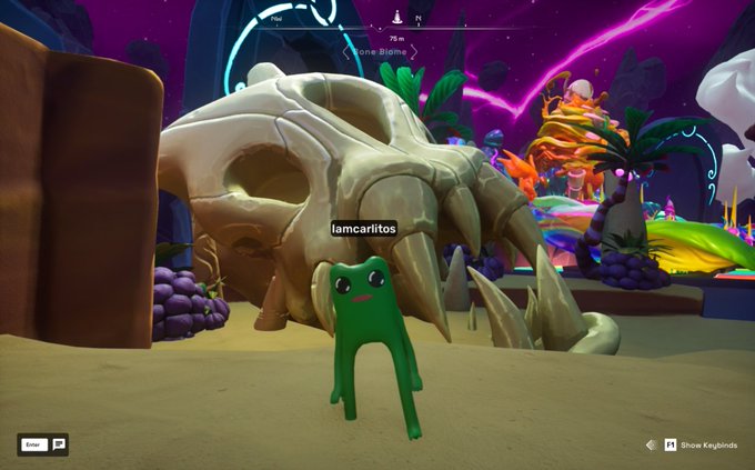 A screenshot from a colorful video game showing a green character named 'iamcarlitos' standing in front of a large skull in a vibrant, alien landscape.