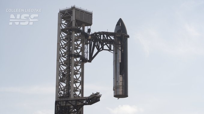 A SpaceX Starship rocket stands on a launch tower against a pale sky, with the text "COLLEEN LIEDTKE NSF" visible in the corner.