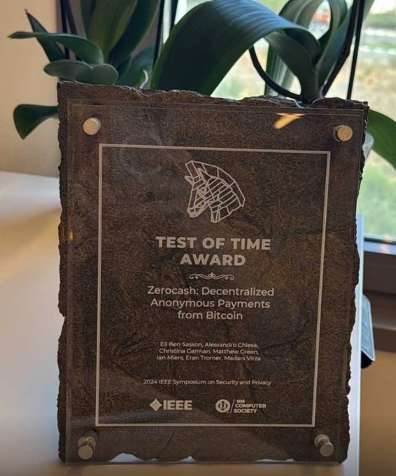 A "Test of Time Award" plaque presented to the authors of "Zerocash: Decentralized Anonymous Payments from Bitcoin" at the 2024 IEEE Symposium on Security and Privacy. The rough stone-style trophy honors the paper by Eli Ben-Sasson, Alessandro Chiesa, Christina Garman, Matthew Green, Ian Miers, Eran Tromer, and Madars Virza for its lasting impact, as noted in the caption about its 10-year recognition.