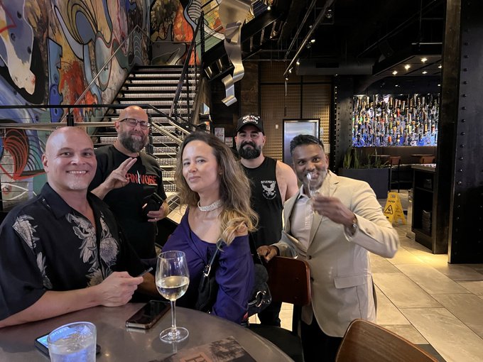 A group of five people poses together at a modern venue with a bar and staircase, smiling for the camera during #nftnyc2026, including NFT legends MarcMauro, MariSMatarazzo, ookaswaka, and NFCreeps as mentioned in the post.