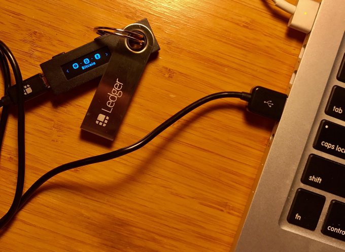 A Ledger hardware wallet for Bitcoin is plugged into a laptop on a wooden desk.