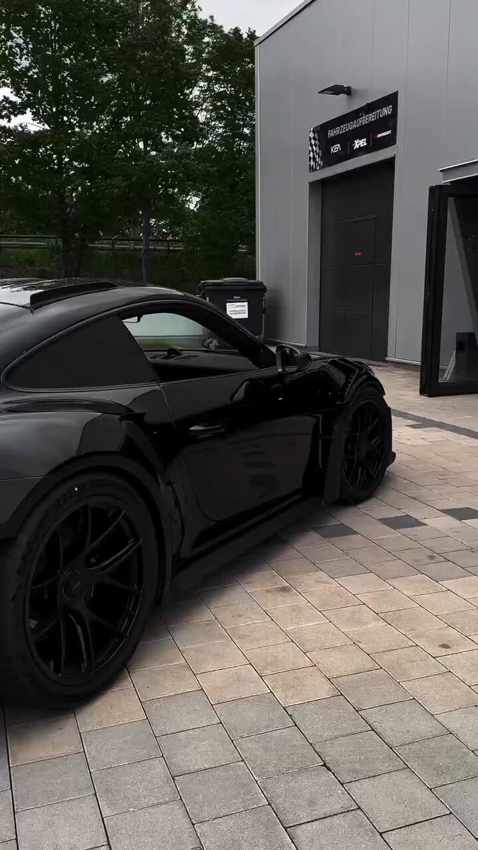 The image features a black sports car parked outside of a building with a gray door. The car has large wheels and a sleek design that suggests it's a high-performance vehicle, possibly a sports car or a luxury sedan. The text "It won'T happen overnight. But if you quit, it won't happen at all." is present in the image, which could be related to the car owner's decision to keep their car parked outside despite potential risks like weather conditions or theft.

The main focus of the image is on the black sports car and its surroundings, with a gray door nearby that contrasts with the car's dark color. The presence of trees in the background adds an element of nature to the scene.