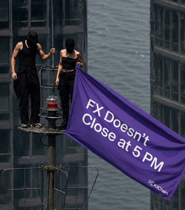 Two people dressed in black stand on a high platform attached to a pole, holding a large purple flag that reads 'FX Doesn't Close at 5 PM' and 'KitChain'.