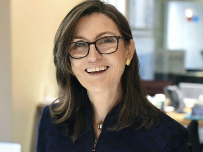 Cathie Wood of Ark Invest smiles in an office setting. The image accompanies news of her firm's trading activity, including a notable $14.1 million purchase of SpaceX shares and a smaller sale of Robinhood stock.
