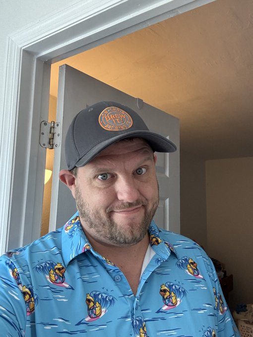 A selfie of a man wearing a gray cap with a 'FRED'S CONTAINER' logo and a blue Hawaiian shirt featuring wave and surfing bear patterns.