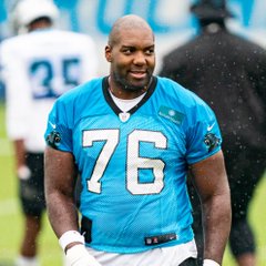 A Carolina Panthers player wearing jersey number 76, identified as Russell Okung, stands on the field in his teal team uniform. The image relates to the post about his 2020 decision to convert half of his $13 million NFL salary into bitcoin through a third-party service.