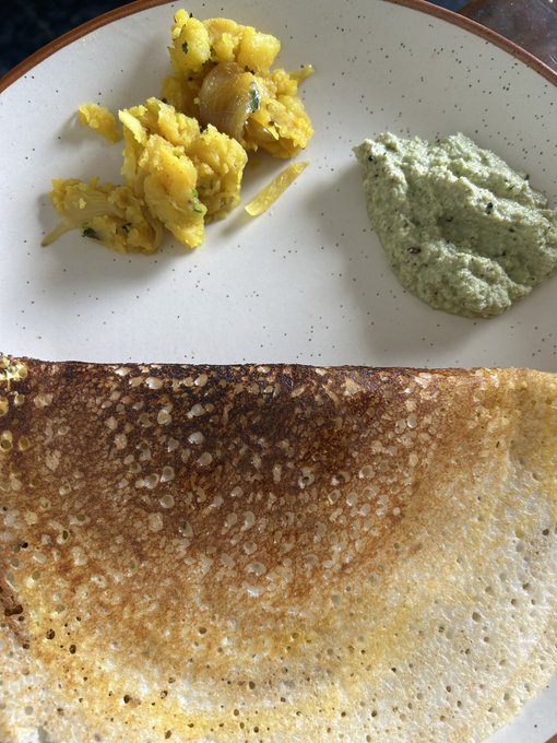 A plate containing scrambled eggs, a green dip or sauce, and a large crispy dosa or pancake.
