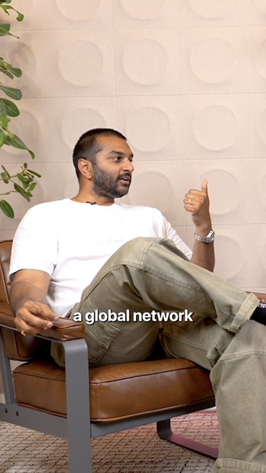 A man with a beard sits in a brown leather chair giving a thumbs-up while speaking, wearing a white t-shirt and green cargo pants, with the caption "a global network" displayed at the bottom of the frame.