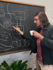 A man with long hair stands in front of a chalkboard covered in mathematical equations and diagrams, including "X=42" and "Carl's brain storm" written on it, while holding up a white mug featuring a Tesla logo, tying into the "New mug alert" post.