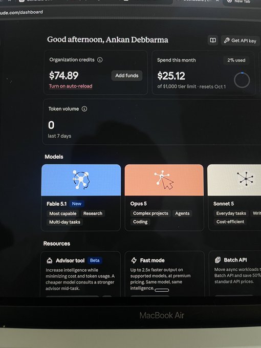 A photograph of a MacBook Air screen displaying the Claude dashboard for "Ankan Debbarma," showing organization credits of $74.89, monthly spend of $25.12, and model options including "Fable 5.1," "Opus 5," and "Sonnet 5."