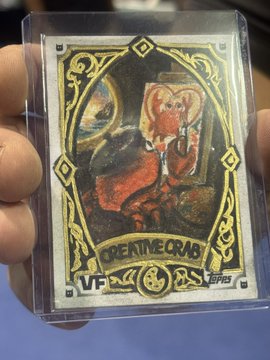 A hand holds a clear plastic trading card or collectible featuring a cartoon crab wearing a red robe and a crown. The card has a gold and black ornate border with the text 'OPERTIME CRAB' and 'VF' at the bottom.