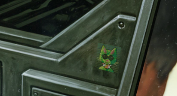 A small green cartoon cat sticker is affixed to a dark green plastic surface.