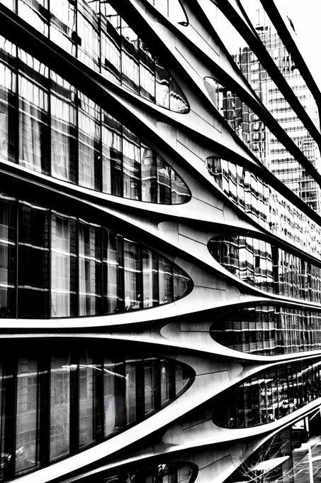 A striking black and white architectural photograph featuring curved, ribbon-like metallic structures with reflective glass surfaces in an urban setting.