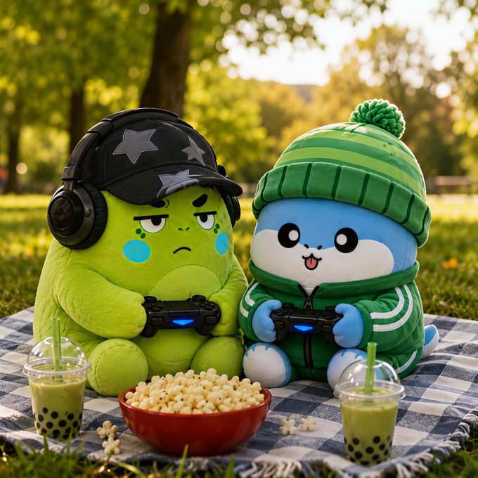 Two cute plush characters—a grumpy green figure with star-patterned headphones and a cheerful blue creature in a green beanie—are enjoying a picnic on a checkered blanket in a sunny park, complete with boba teas and a bowl of popcorn as they play video games together. 

The image contrasts with the post's message about *Sleepagotchi*, which promotes healthier habits like better sleep instead of endless screen time and gaming, suggesting a shift from sedentary entertainment to more mindful, restorative routines.