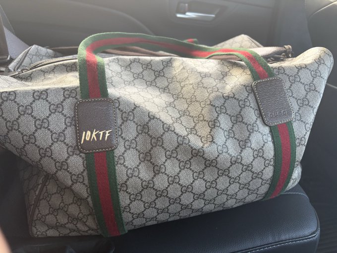 A Gucci monogram duffle bag with the signature green and red stripe, featuring a leather tag with '10KTFF' written in yellow.