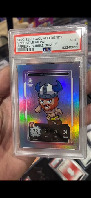 A hand holds a PSA-graded trading card labeled '2022 ZEROCOOL VEEFRIENDS VERSATILE VIKING SERIES 2 - BUBBLE GUM 1/1 MINT 9' featuring a cartoon Viking character with stats (Score 73, Arm 25, Skill 24, Stamina 24) on a holographic background.