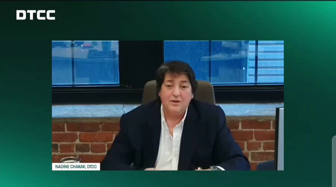 The image shows a woman sitting at a desk, wearing a suit and talking into a microphone during an online meeting or presentation. The background of the image features a green wall with windows that allow natural light to enter the room. The caption on the image reads "Probably Nothing...DTCC'S Nadine Chakar says tokenization is no longer a concept or pilot. It's moving from proof of concept to proof of value; mobilizing assets, unlocking liquidity, and scaling across the ecosystem with a participant group ready to prove it $XLM $XRP $CC".