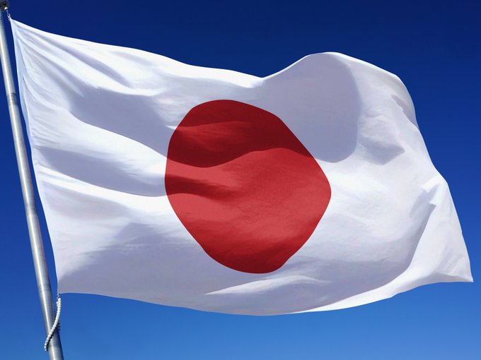 The image shows the Japanese flag—a white flag with a red circle—waving against a clear blue sky. The post references Japan advancing toward approving Bitcoin ETFs, and the flag visually represents the country at the center of this regulatory development.