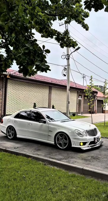 A white Mercedes-Benz sedan with aftermarket wheels sits parked on a residential street, its dealer plate partially visible. The scene suggests a low-budget car listing or sale, contrasting with the post's commentary on how easily reputations can be damaged over small profits—perhaps implying the seller quickly parted with the car for marginal gain.