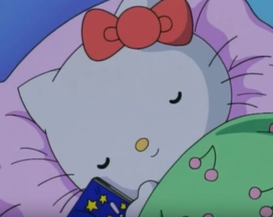 Hello Kitty wearing a red bow, sleeping peacefully with closed eyes next to a green pillow with cherry designs.