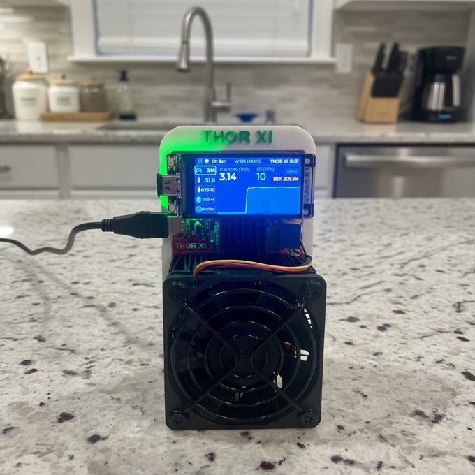 A small electronic device labeled "THOR XI" with a small display screen showing cryptocurrency mining data ("Multipool (TNN)"), placed on a granite kitchen countertop with a cooling fan.